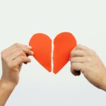 يدان تمسكان بنصفين من قلب ورقي ممزق يرمز إلى الانفصالو الطلاق